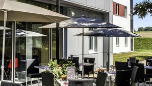 Een terras met tafels en stoelen, parasols en een gebouw op de achtergrond.
