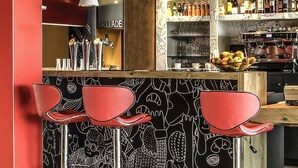 Een bar met rode barkrukken, een toonbank met tappunten en een muur met zwart-wit illustraties.
