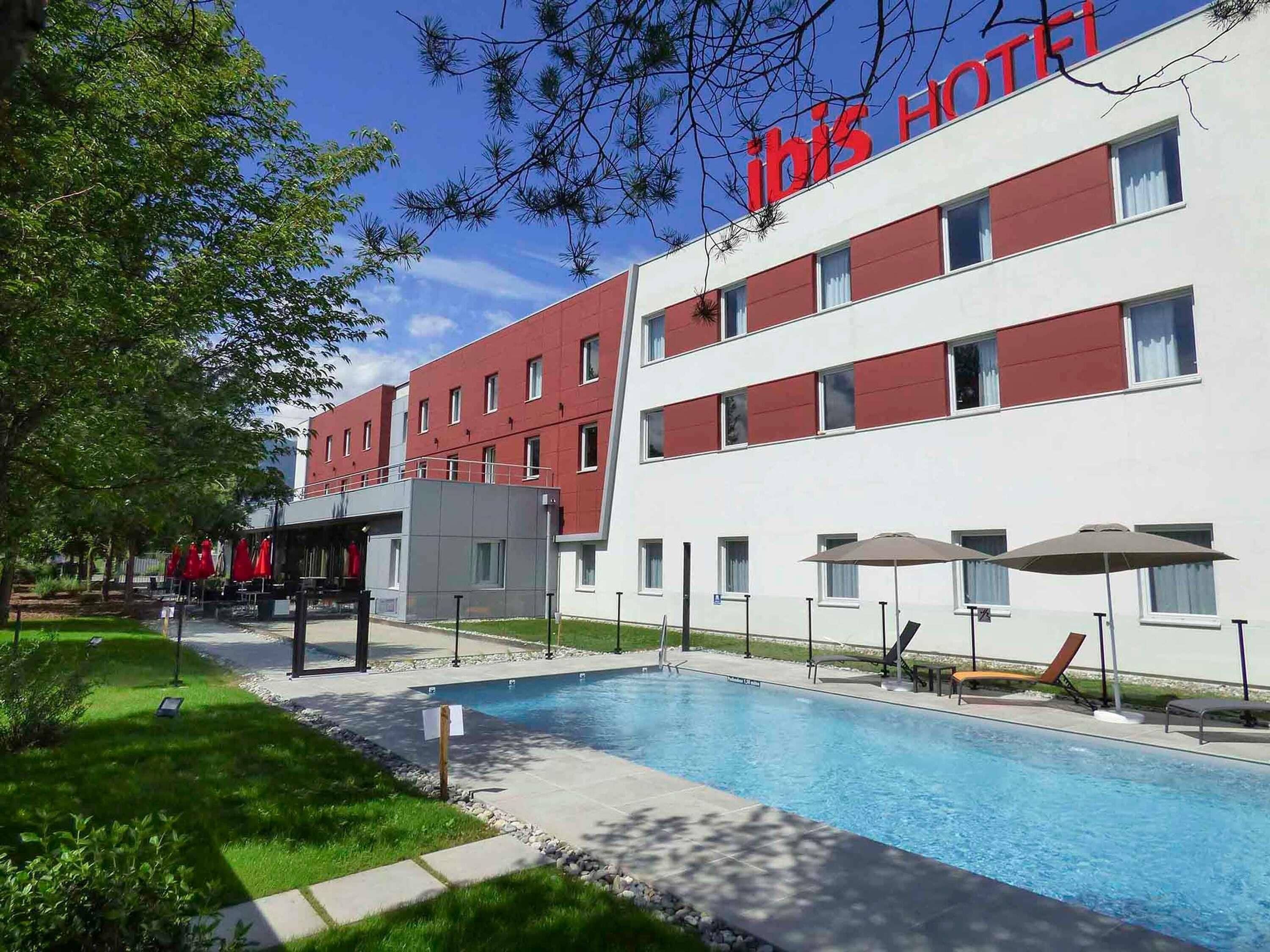 A hotel with a swimming pool, outdoor seating, and a red and white facade.