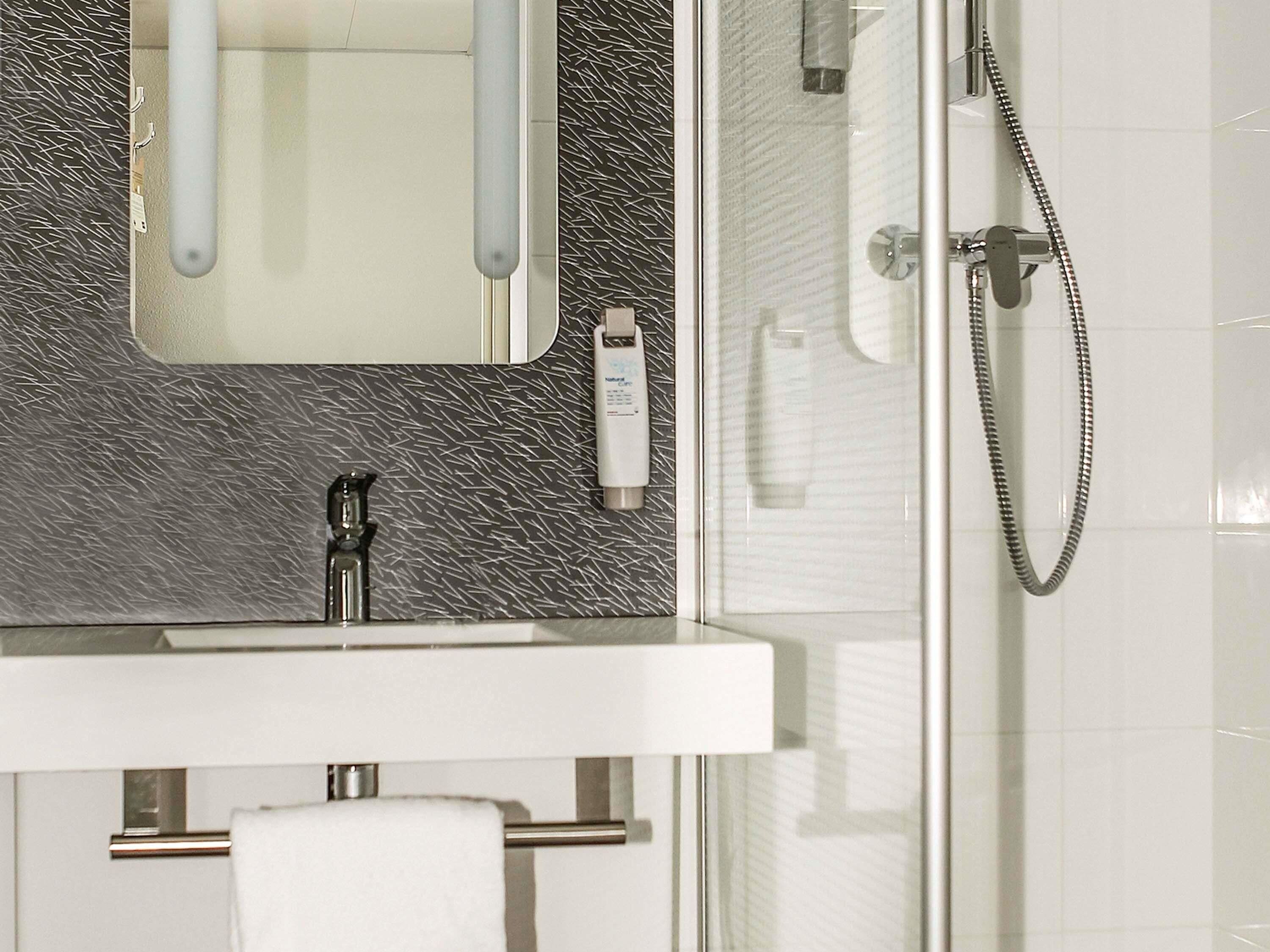 Un baño con cabina de ducha de vidrio, un lavamanos blanco y un perchero para toallas.