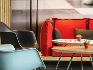 A modern seating area with a round table, two potted plants, and a red sofa.