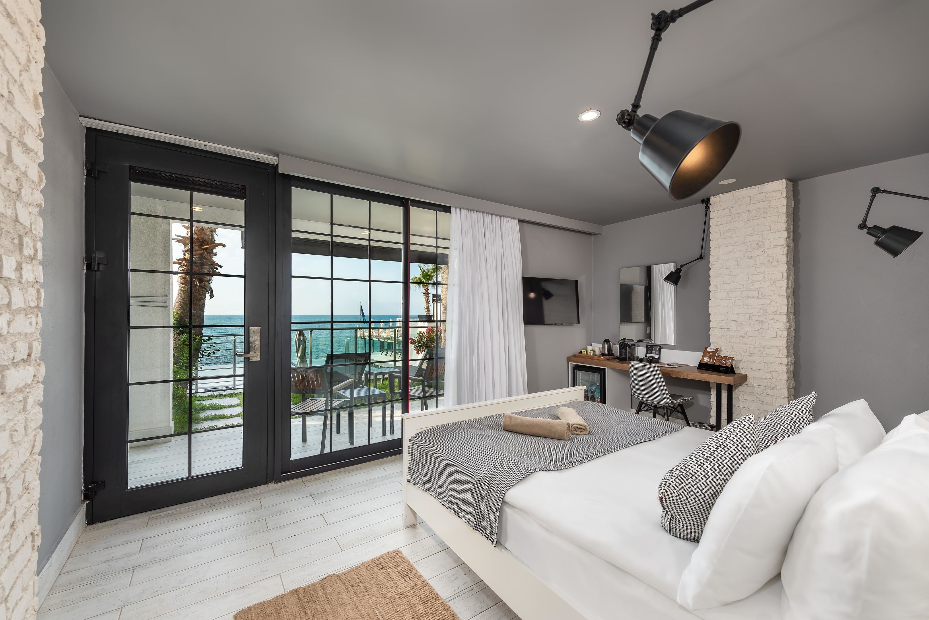 Un dormitorio con cama, escritorio, silla y vista al mar a través de amplios ventanales.