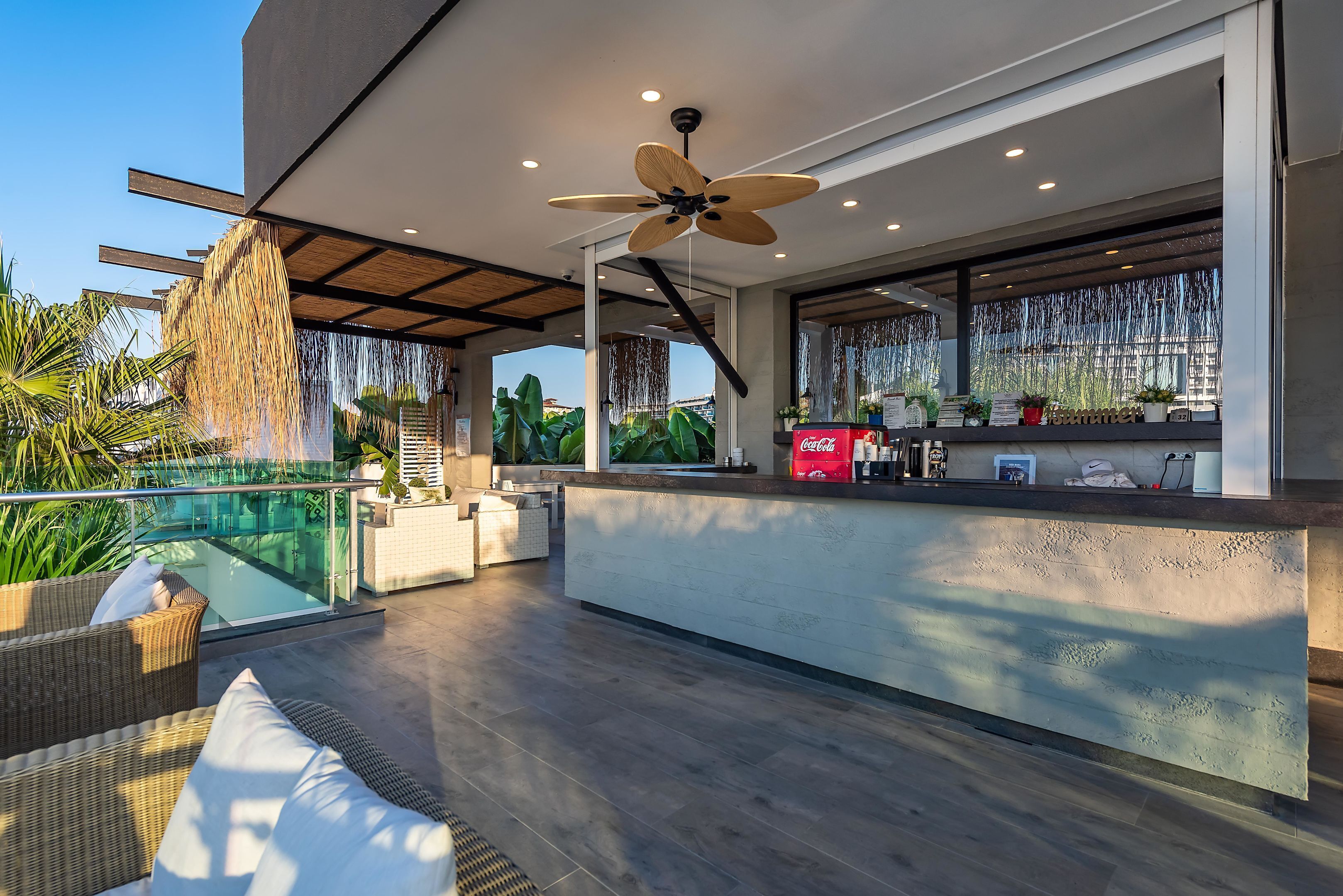 A modern outdoor area with a pool, seating, a bar, and a ceiling fan.