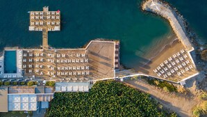 Vista aérea de un hotel frente al mar con varias piscinas, una zona de playa y un litoral rocoso.