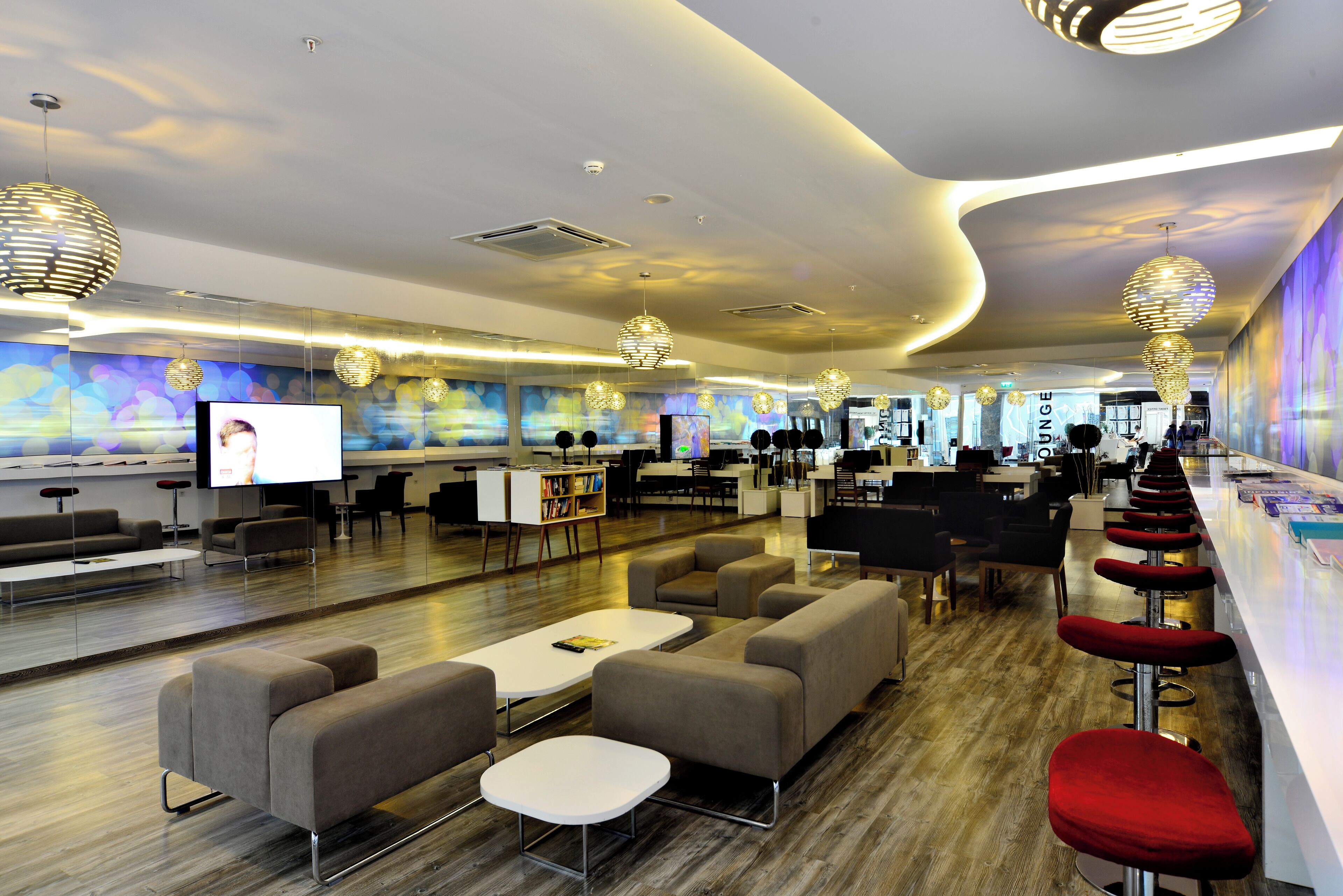 A modern lounge area with sofas, tables, and a bar with red stools.