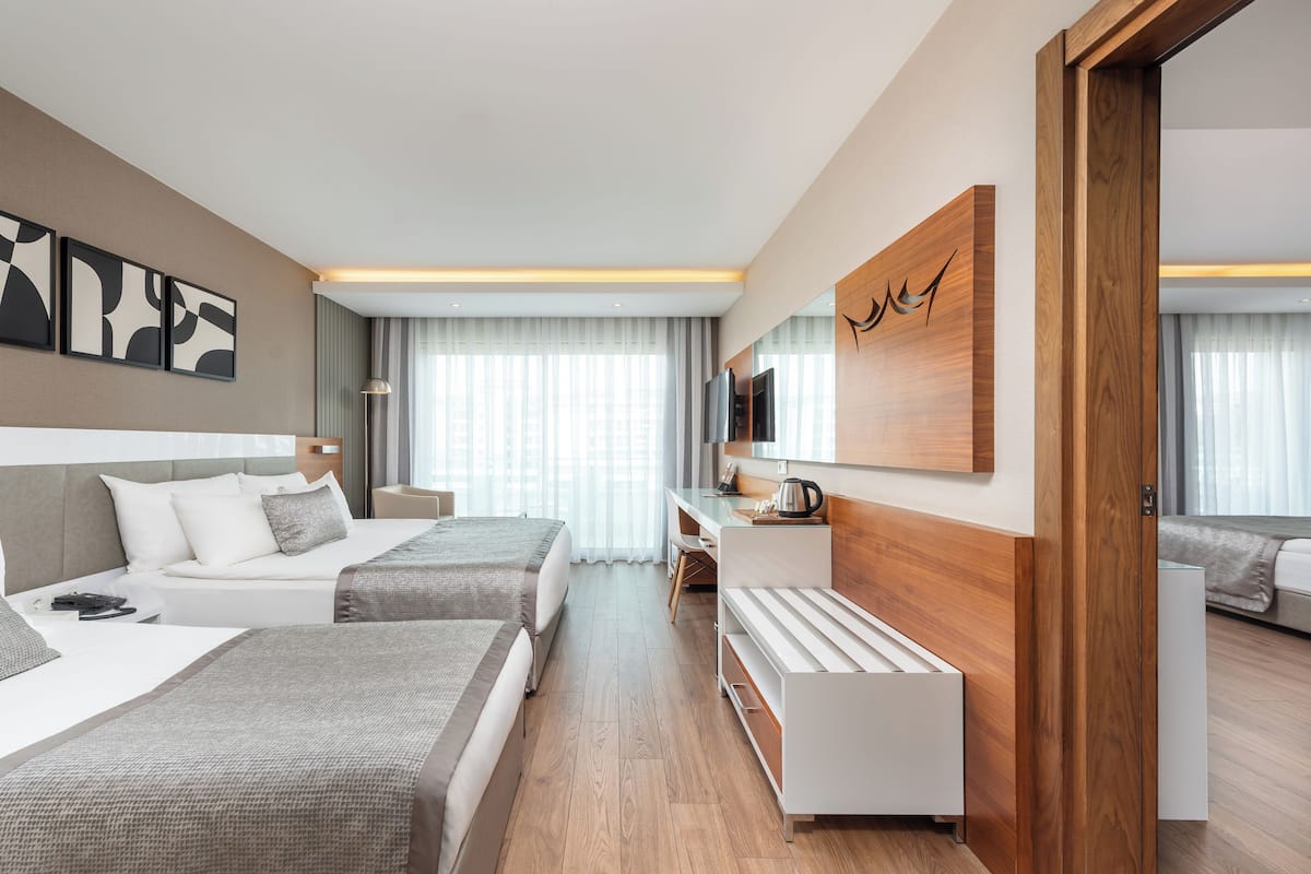 A modern hotel room with two beds, a desk, a TV, and a large mirror.