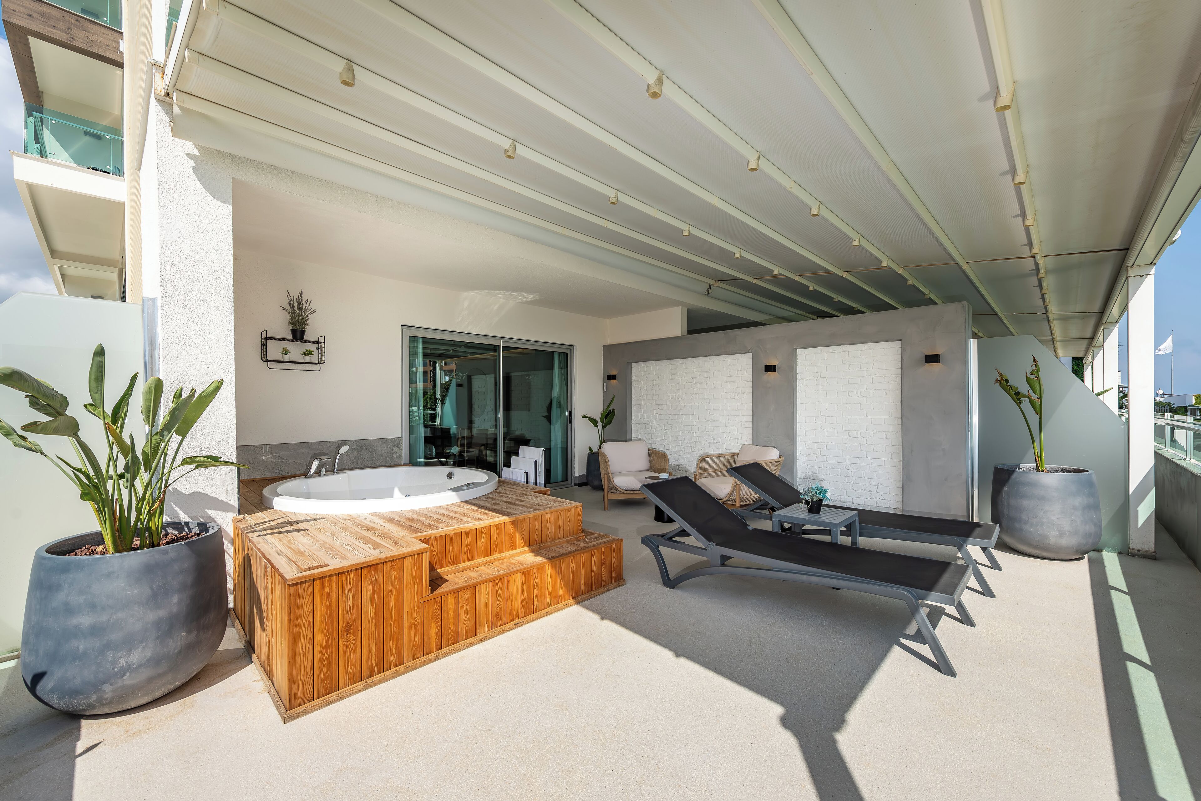 A modern outdoor area with a wooden hot tub, lounge chairs, and potted plants.