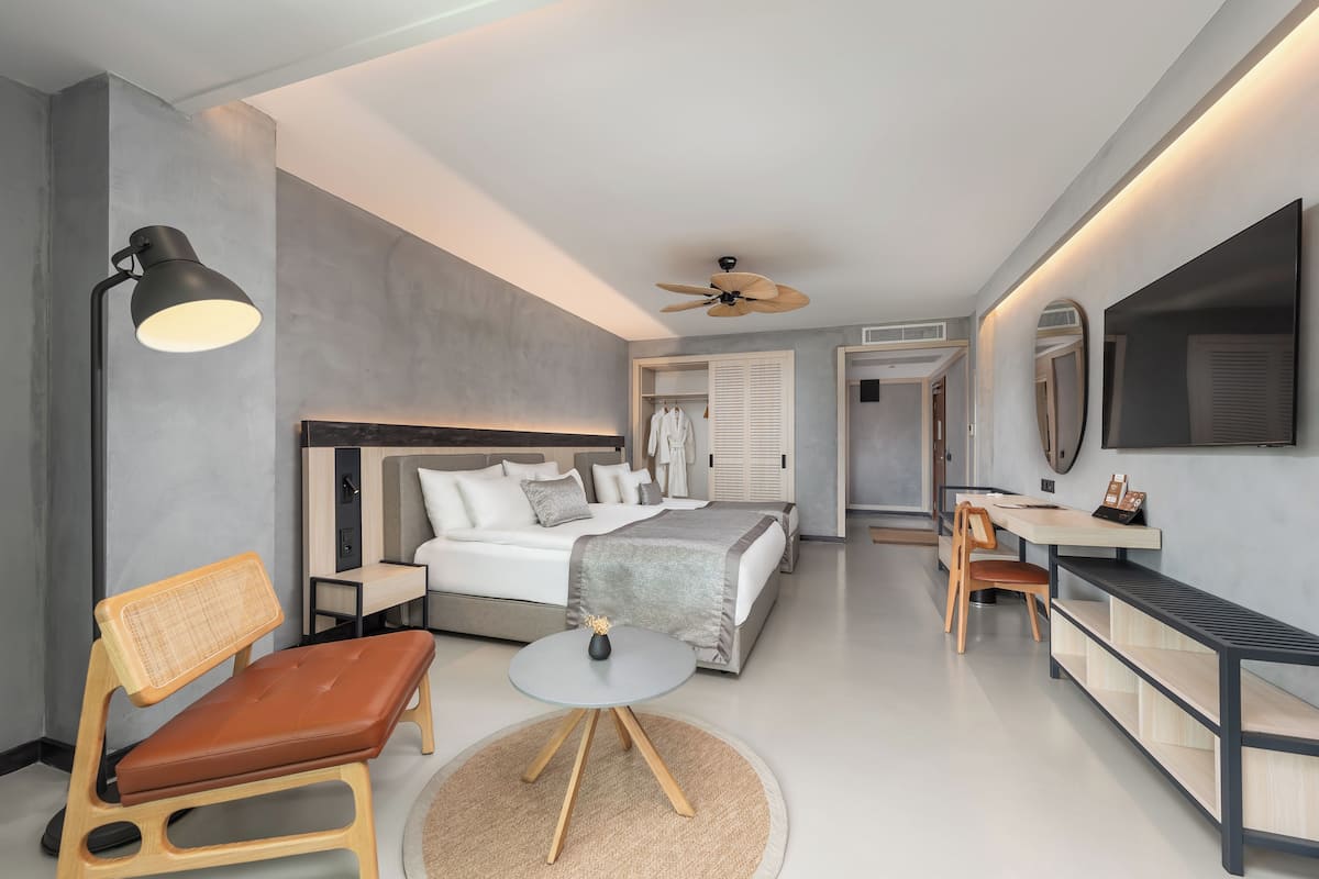 A modern hotel room with a bed, bedside table, chair, desk, and a television.