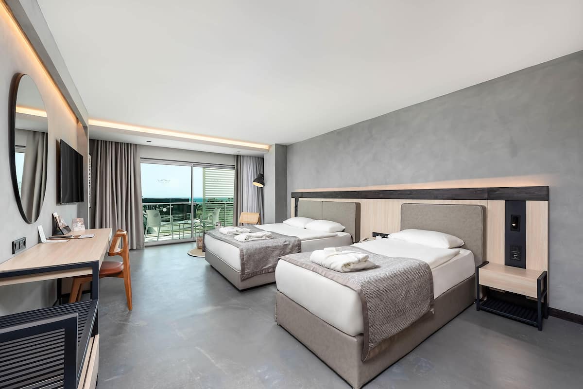 A modern hotel room with two beds, a desk, and a balcony with a view.