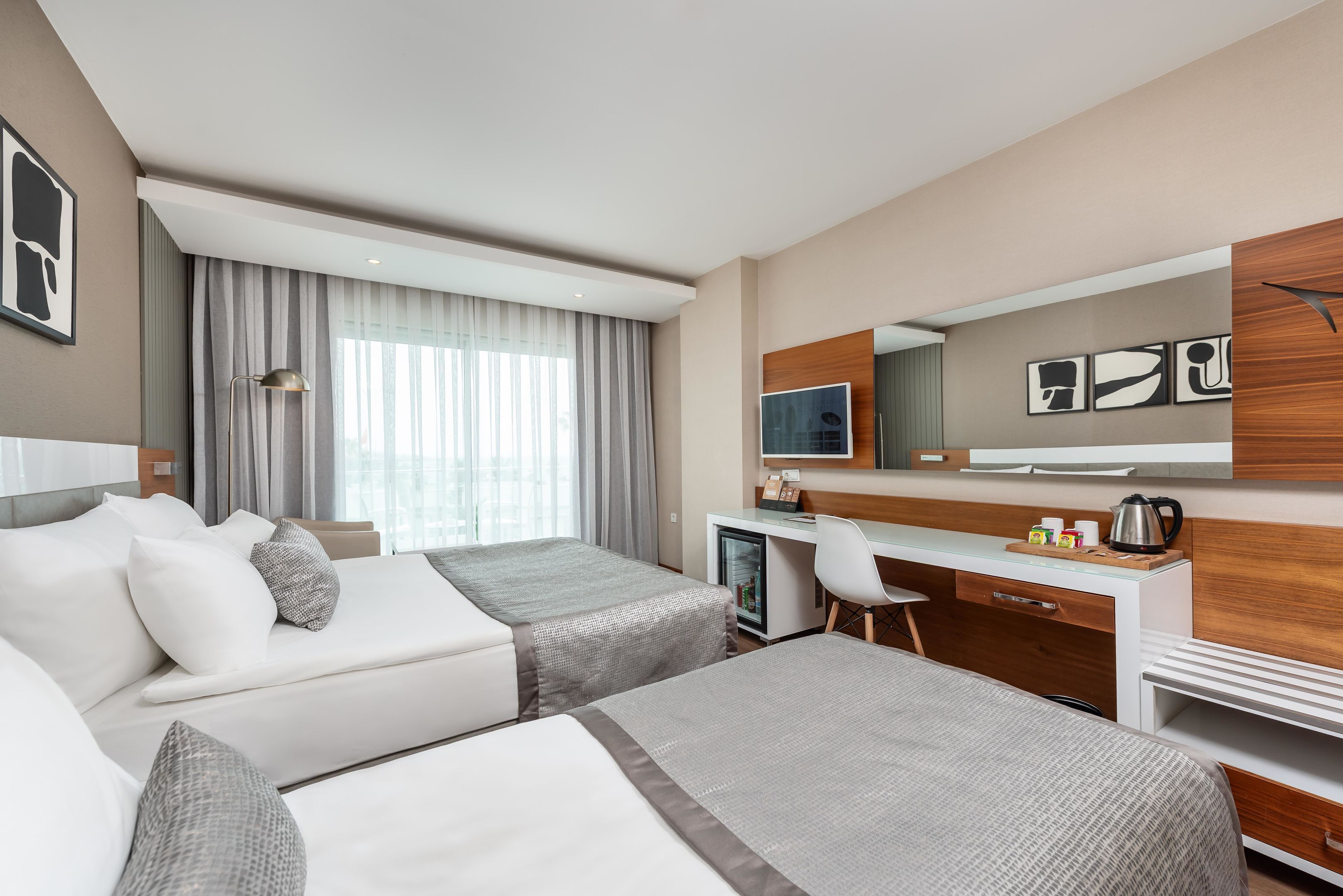 Quarto de hotel com duas camas, uma escrivaninha, uma cadeira, uma televisão e um minibar.