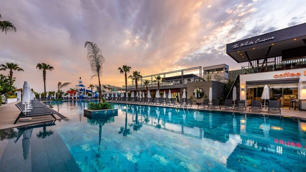 Una piscina con sillas de descanso, un tobogán acuático y un restaurante llamado 'The White Cuisine'.