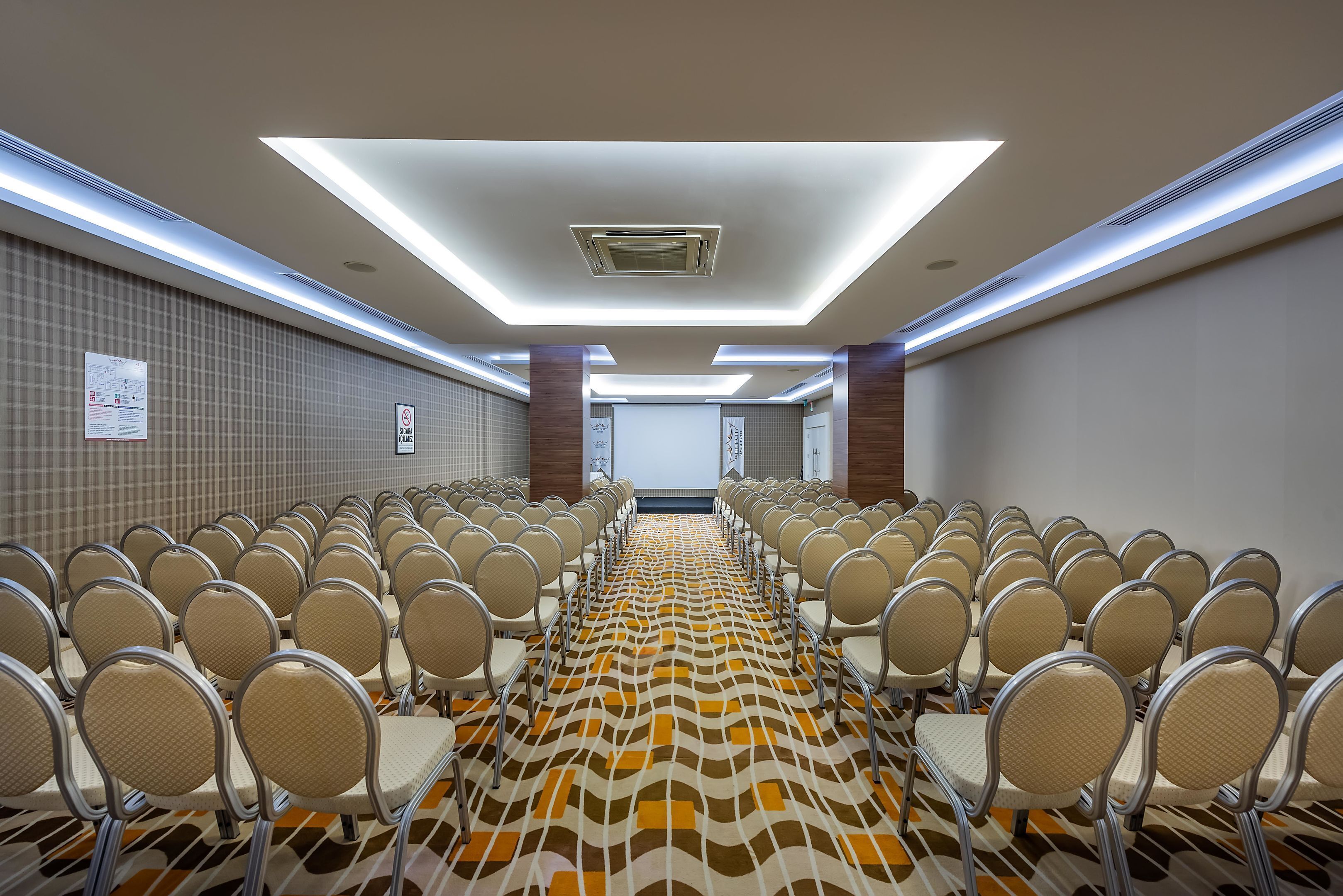 A conference room with rows of chairs, a patterned carpet, and a ceiling with recessed lighting.
