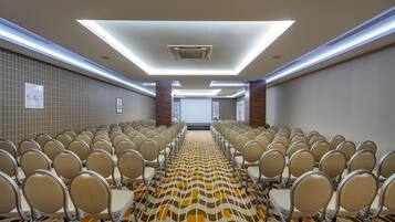 A conference room with rows of chairs, a patterned carpet, and a ceiling with recessed lighting.