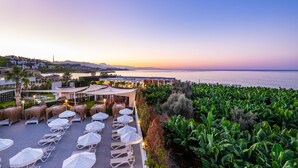 Une terrasse sur le toit, dotée de chaises longues et de parasols, offrant une vue sur le paysage urbain côtier et la mer.