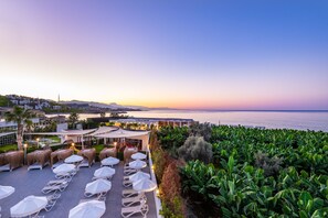 Terraço no telhado com espreguiçadeiras e guarda-sóis, com vista para a cidade costeira e o mar.