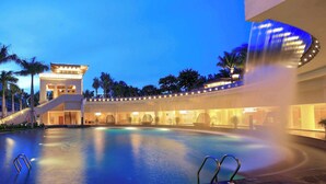 Une grande piscine intérieure dotée d’une cascade, entourée de palmiers et bordée d’un bâtiment à plusieurs étages et agrémenté de balcons.