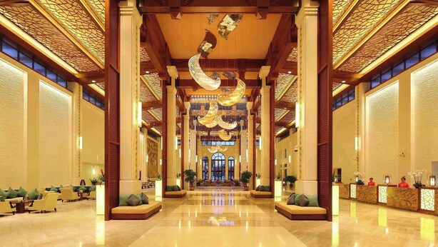 Un hall d’entrée spacieux avec un comptoir d’accueil central, des espaces détente et un plafond décoratif.