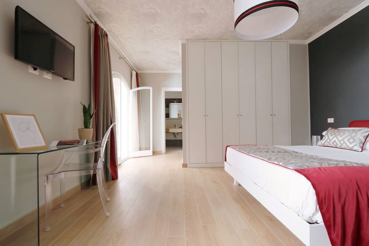 A modern bedroom with a bed, a TV mounted on the wall, a glass table, and a wardrobe.