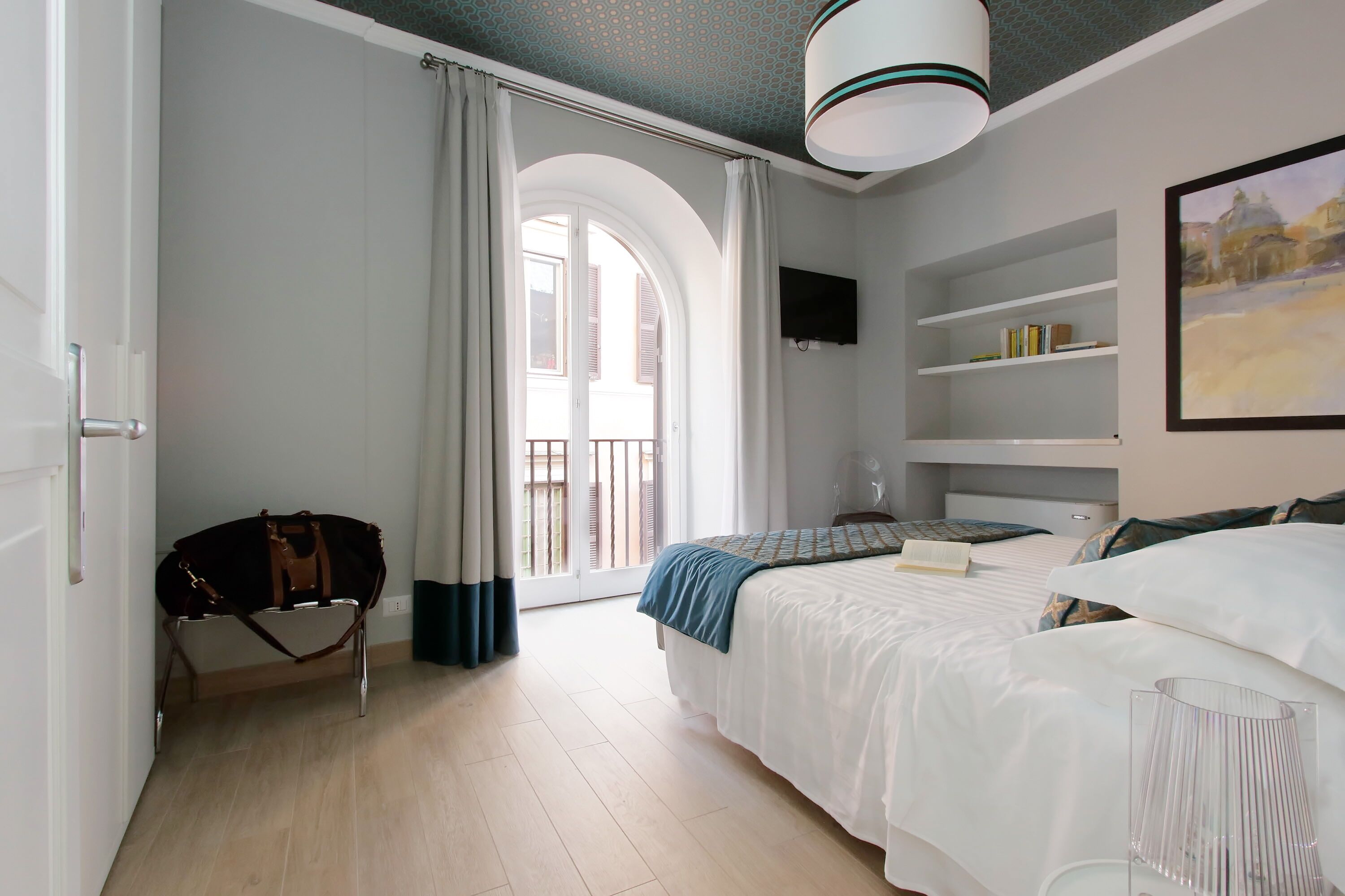 A modern hotel room with a bed, a wardrobe, a desk, a chair, a TV, and a balcony with curtains.