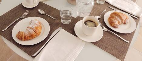 A breakfast setting with croissants, coffee, and a newspaper on a glass table.