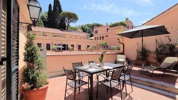 An outdoor patio with a table and chairs, surrounded by potted plants and a large umbrella.