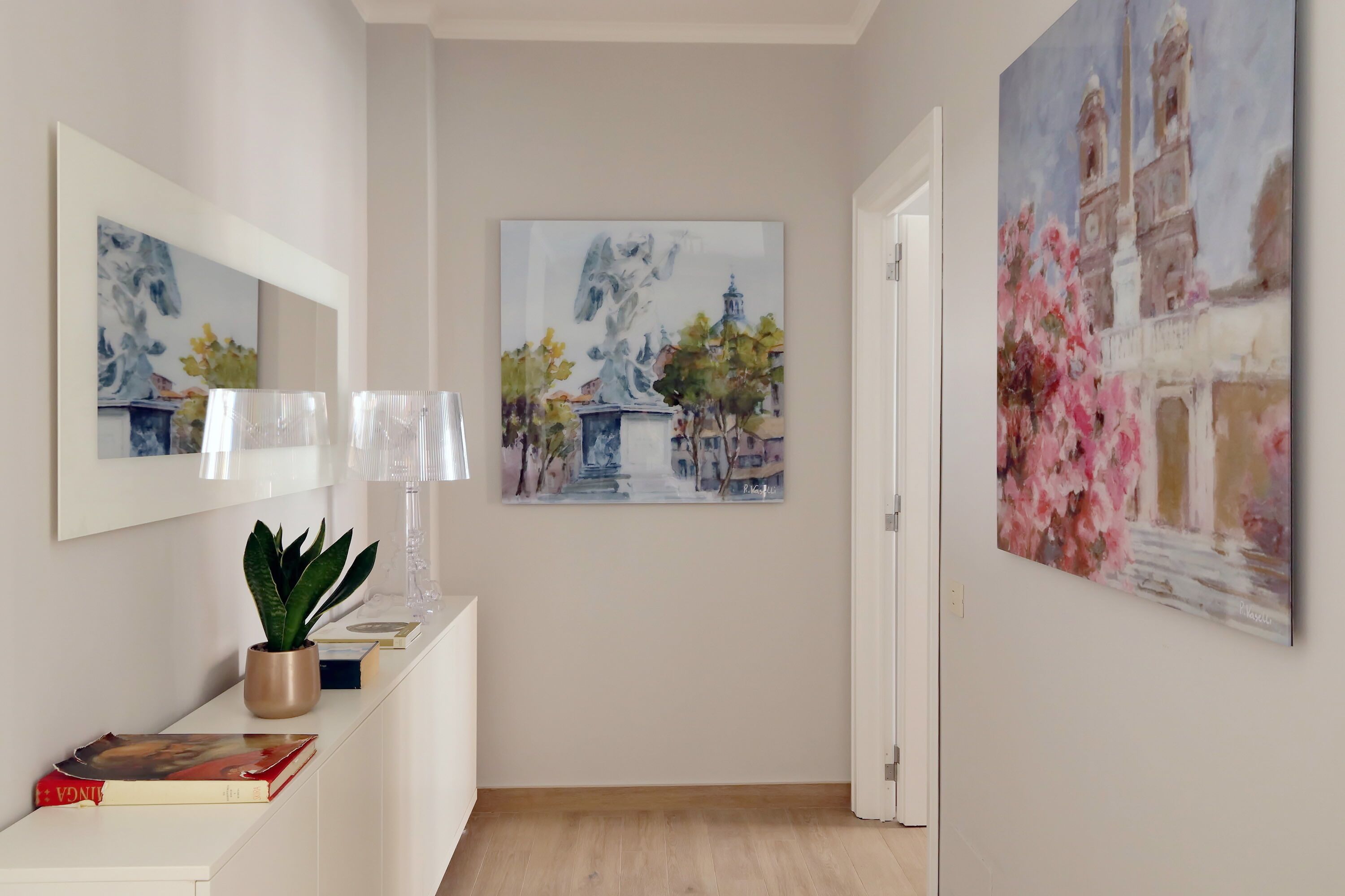 A hallway with a white console table, a potted plant, and two framed paintings depicting architectural scenes.