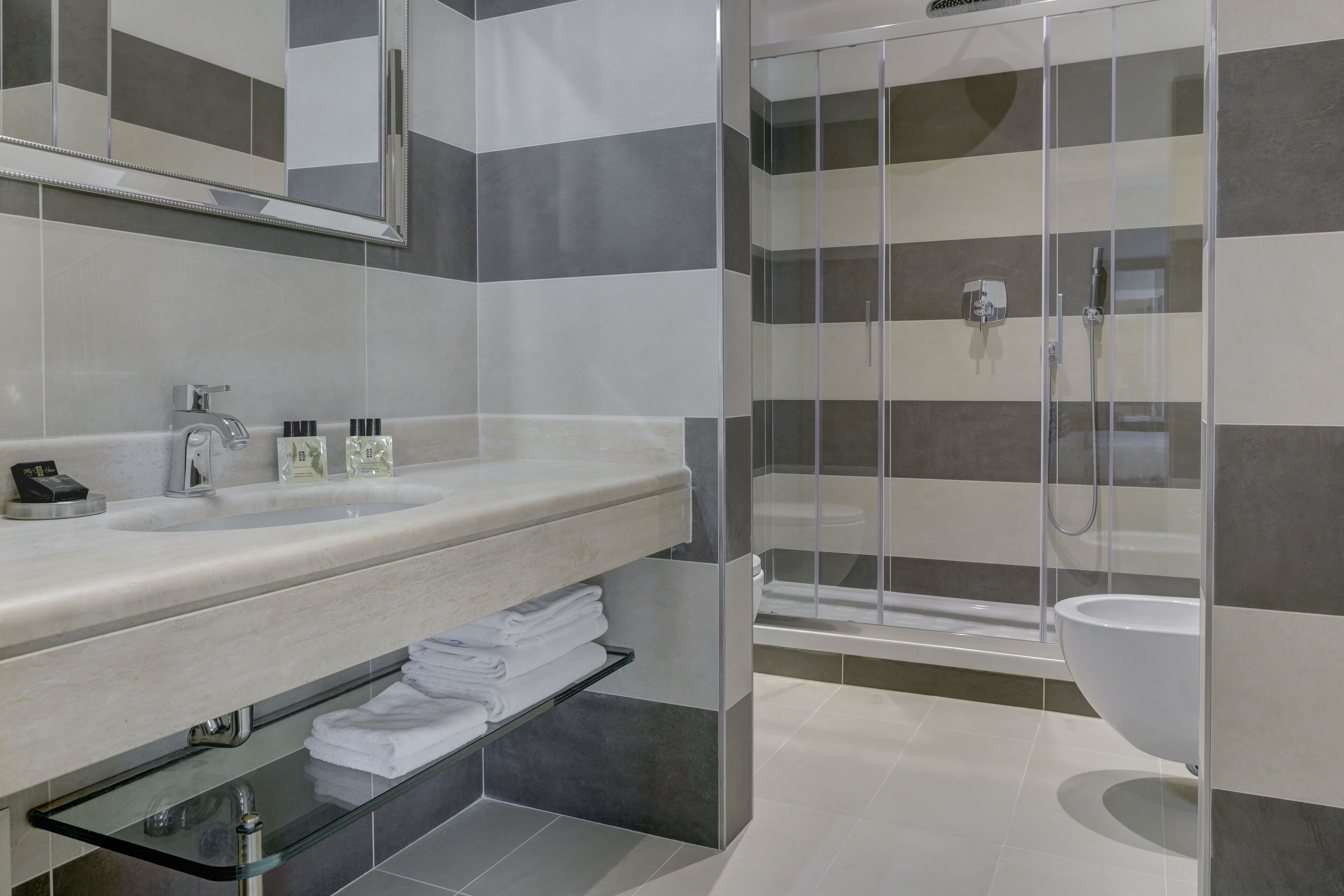 Uma casa de banho moderna com cabine de duche em vidro, um espelho grande e bancada com produtos de higiene pessoal.