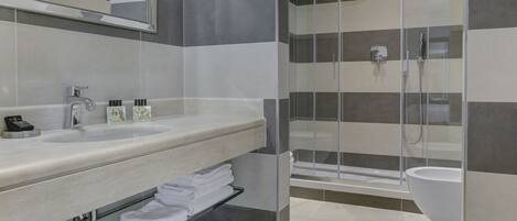 Uma casa de banho moderna com cabine de duche em vidro, um espelho grande e bancada com produtos de higiene pessoal.