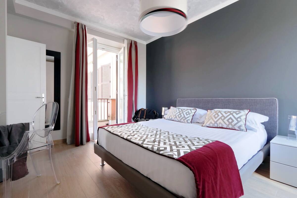 A modern bedroom with a bed, a nightstand, a chair, and a window with curtains.