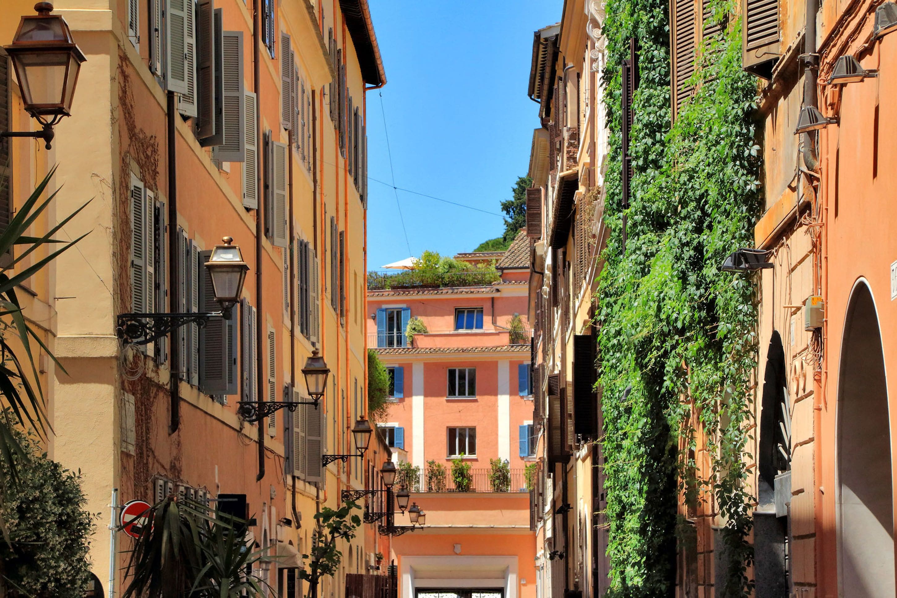 A narrow street with buildings on either side, featuring balconies and a clear blue sky.