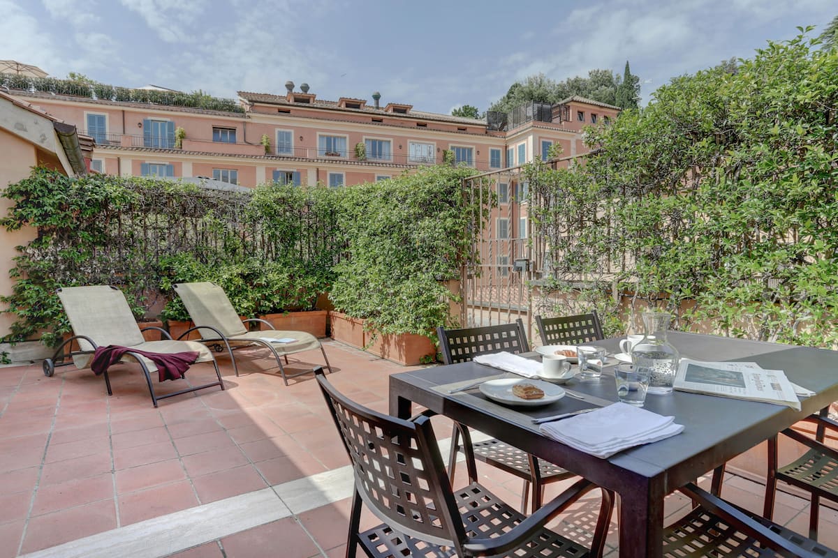 An outdoor patio with a table set for dining, surrounded by chairs and potted plants.