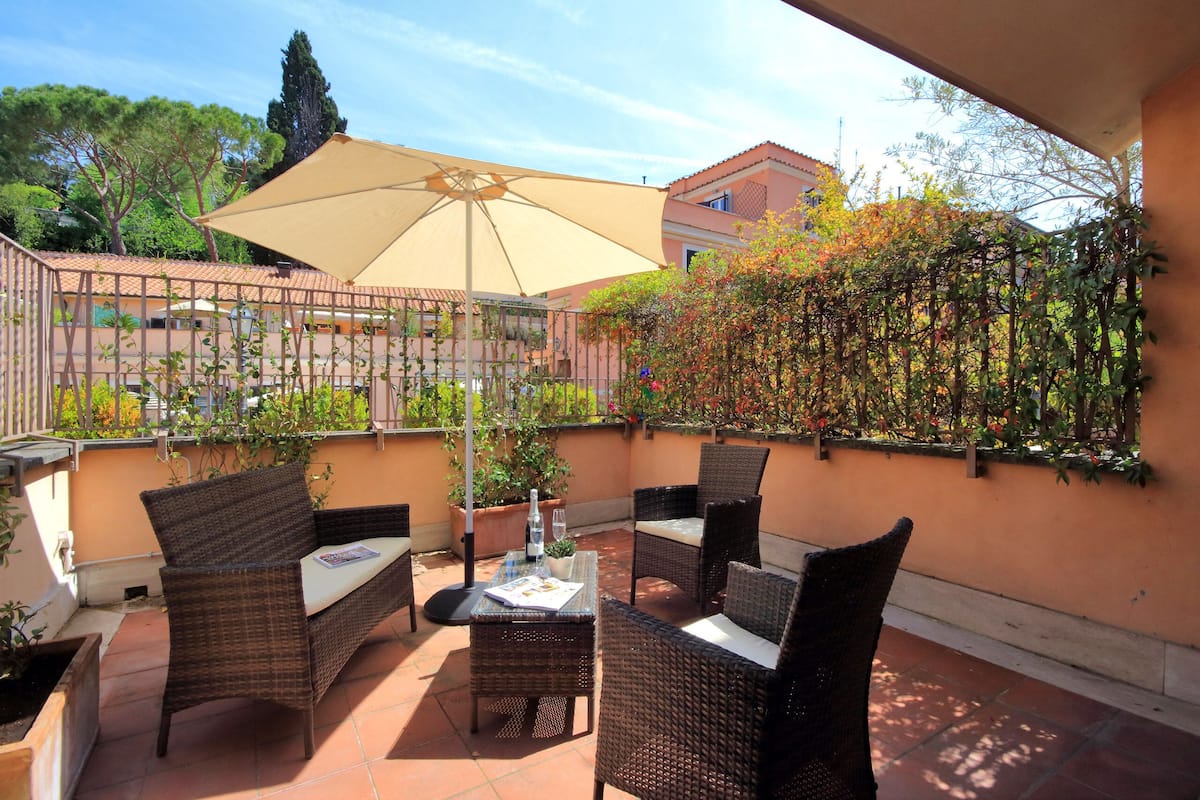 An outdoor patio with wicker furniture, a table, and a large umbrella.