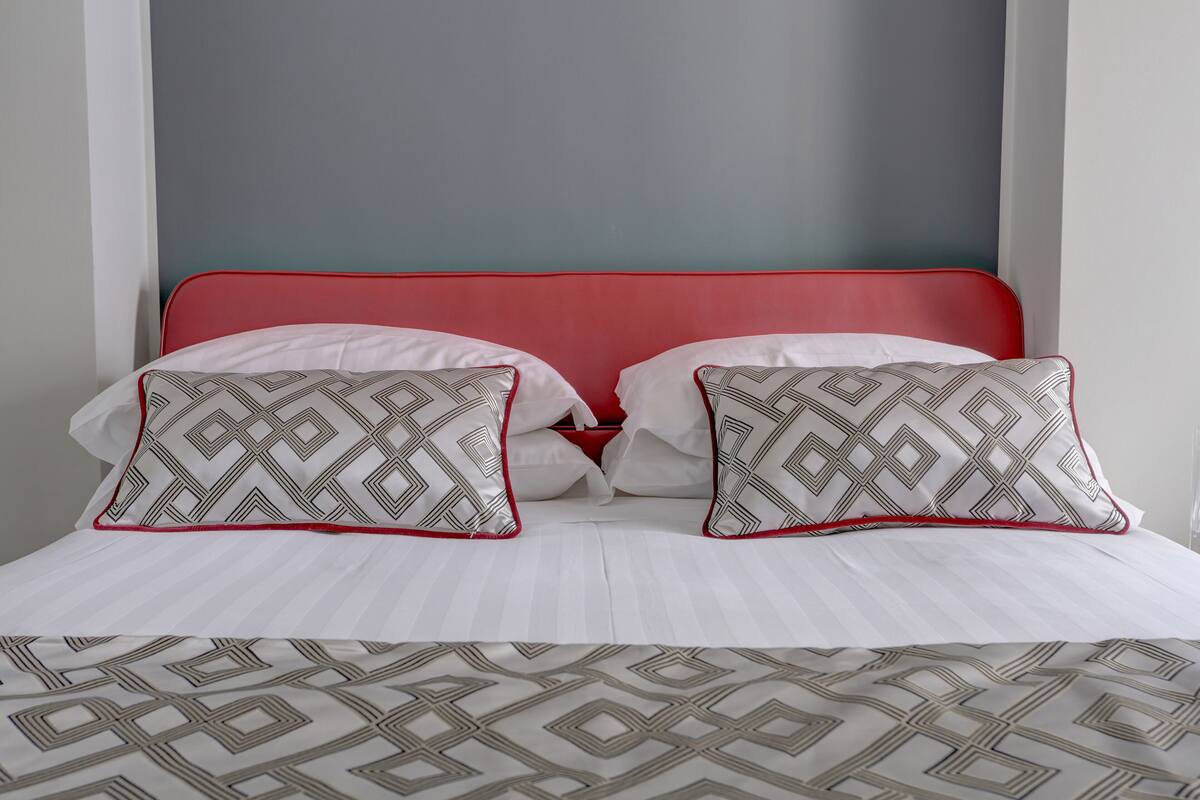 A bed with a red headboard, white bedding, and patterned pillows.