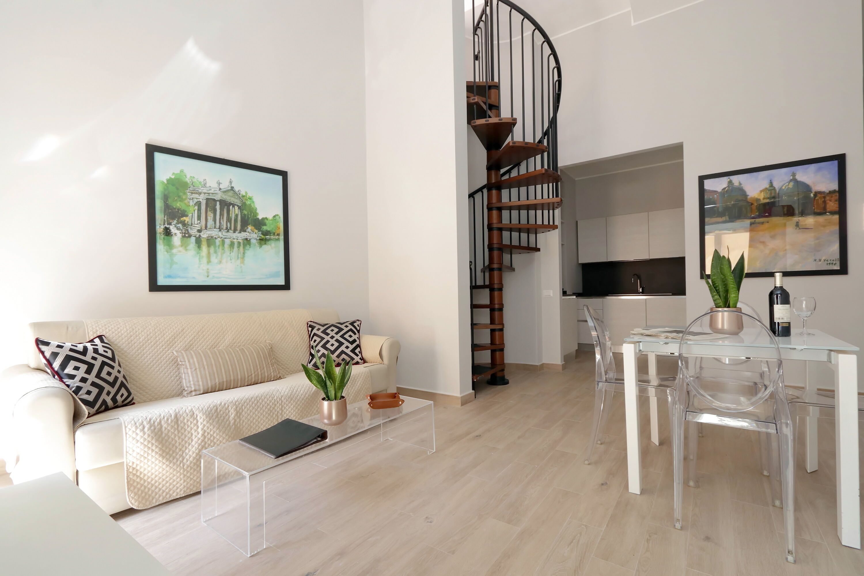 A modern living room with a sofa, coffee table, and clear dining table with chairs. A spiral staircase leads to an upper level.