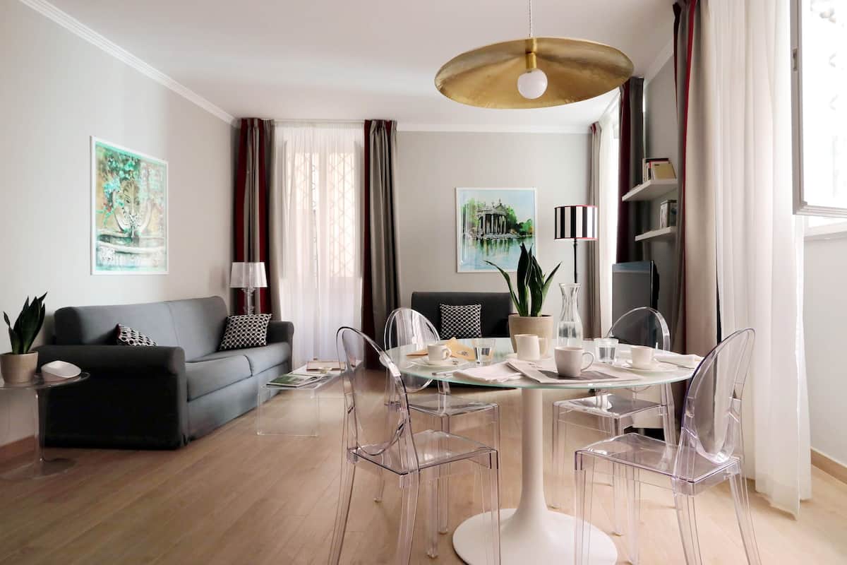 A modern living room with a glass dining table, clear chairs, a grey sofa, and a coffee table.