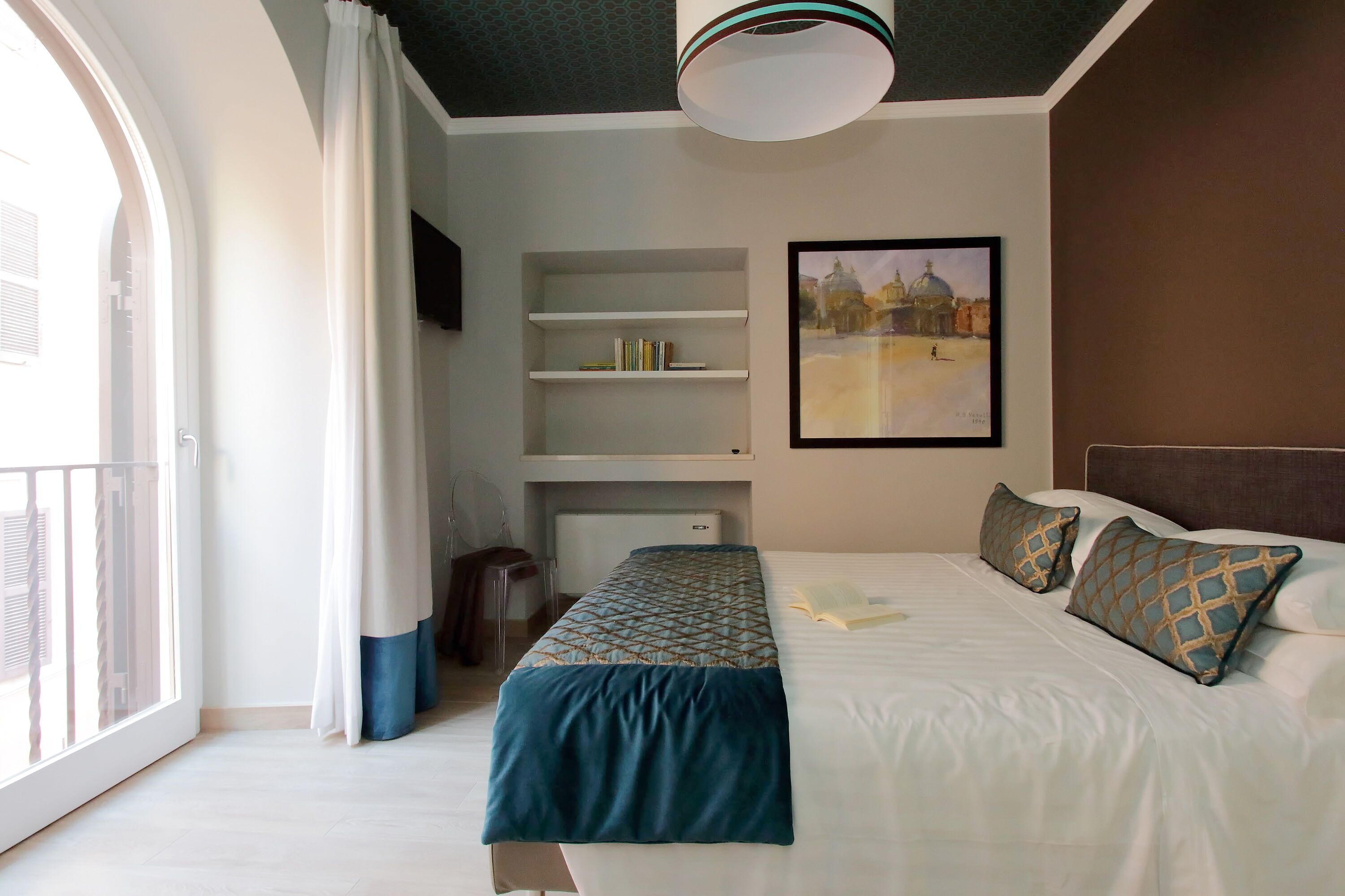 Una camera d'albergo con un letto, una libreria, un quadro e una finestra con tende.
