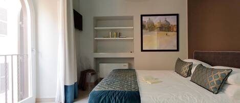 A hotel room with a bed, a bookshelf, a painting, and a window with curtains.