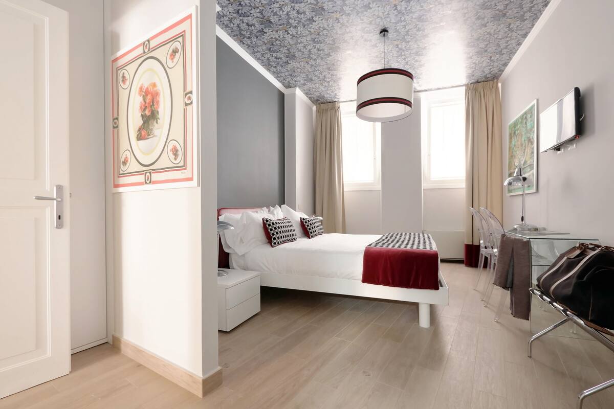 A modern bedroom with a bed, bedside table, and a desk with chairs.