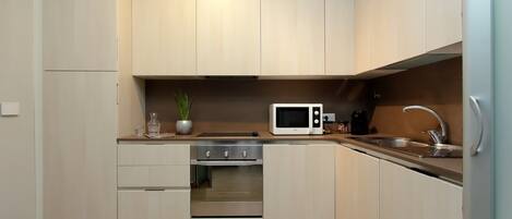 A modern kitchen with light wood cabinets, a stainless steel oven, a microwave, and a sink.