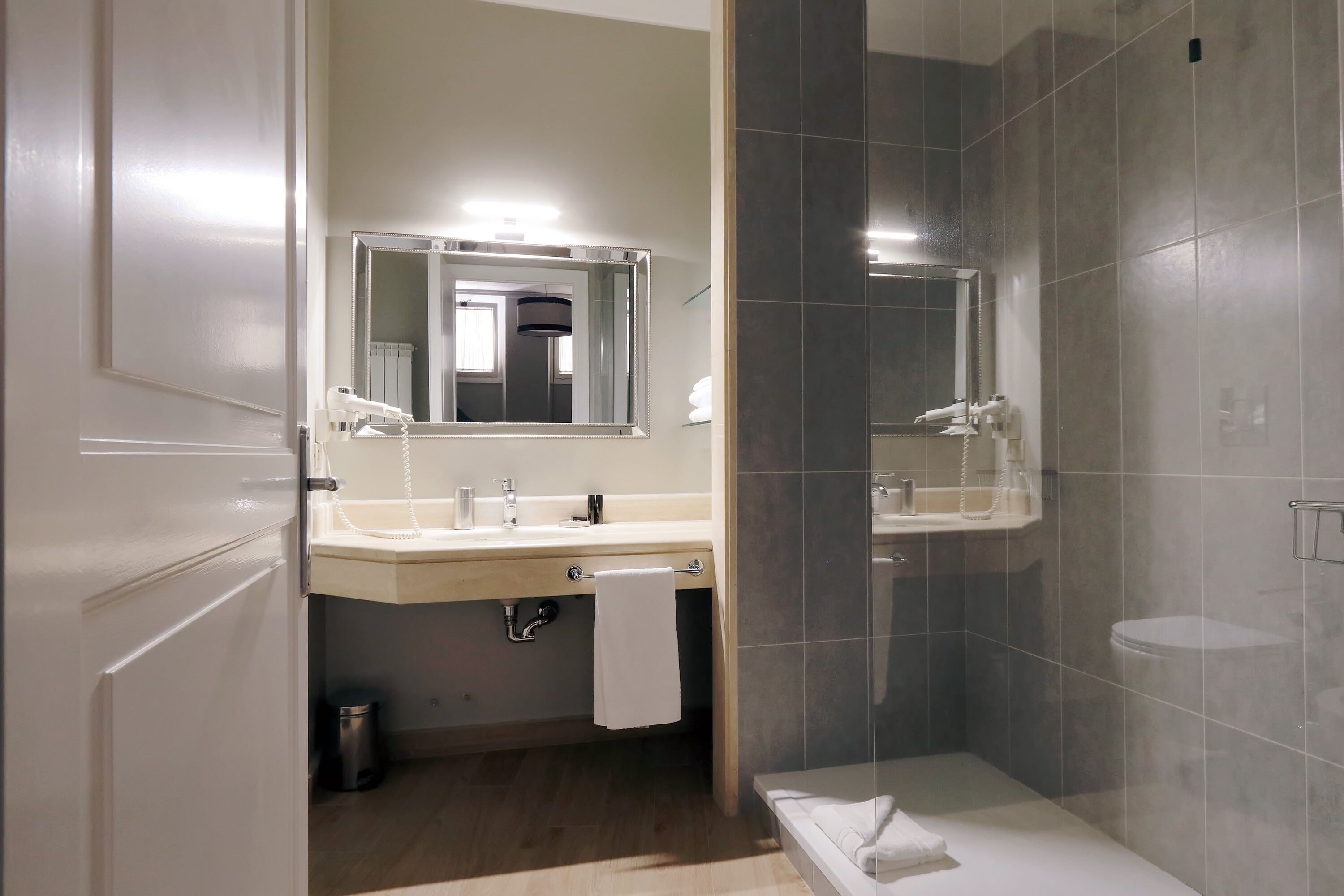 A modern bathroom with a large mirror, two sinks, a shower, and a toilet.
