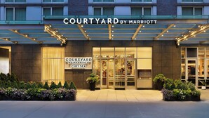 Het uiterlijk van het Courtyard by Marriott Chelsea hotel, met een glazen entree, borden en verzorgde beplanting.