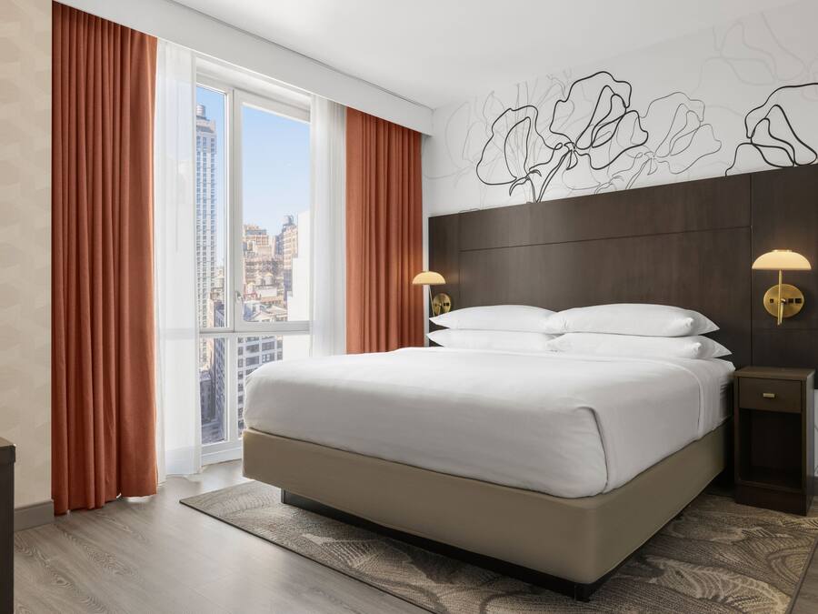 Una habitación de hotel moderna con una cama grande, vistas a la ciudad y un detalle decorativo en la pared.