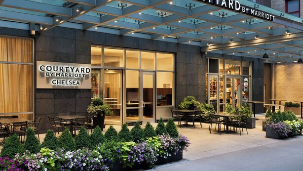 De buitenkant van het Courtyard by Marriott Chelsea hotel met terras en een goed verlichte entree.
