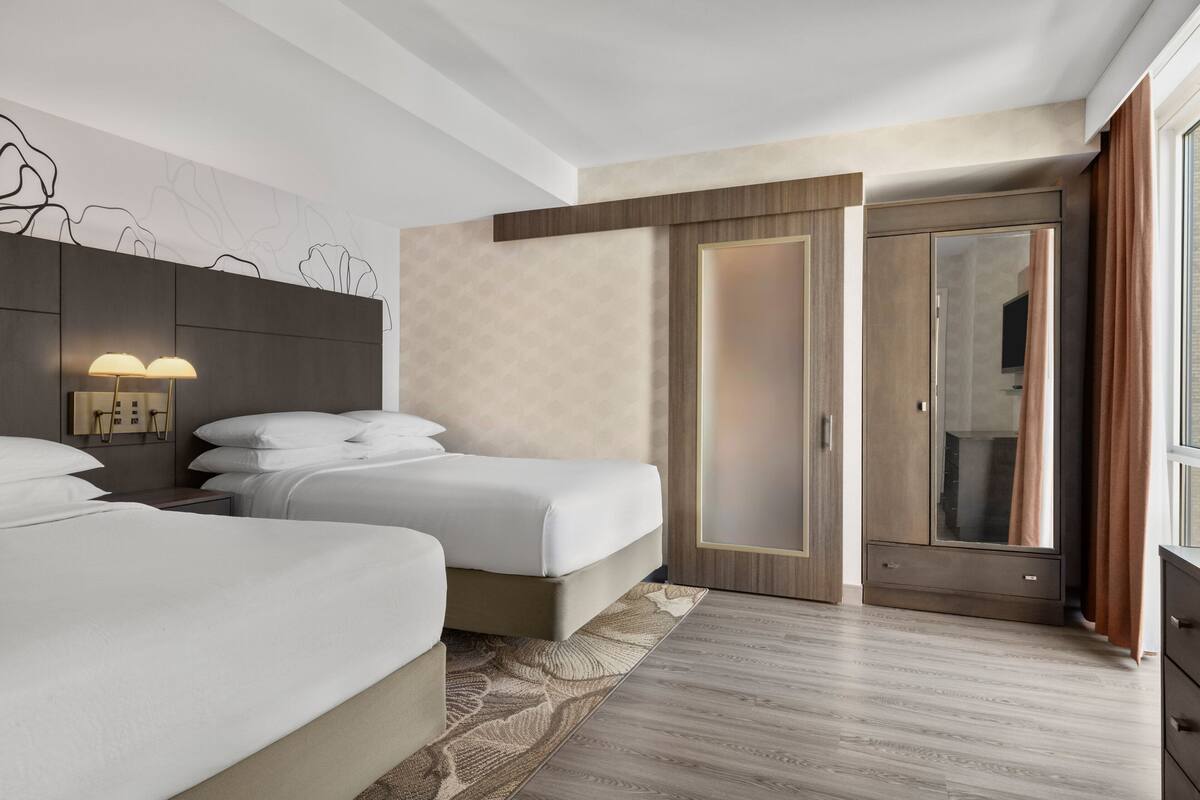 Ein modernes Hotelzimmer mit zwei Betten, einem großen Spiegel und einem Kleiderschrank.