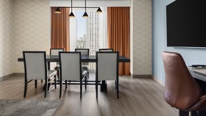 Een moderne eetruimte met een zwarte tafel en zes stoelen, een bruine lederen fauteuil en een stadszicht door grote ramen met bruine gordijnen.