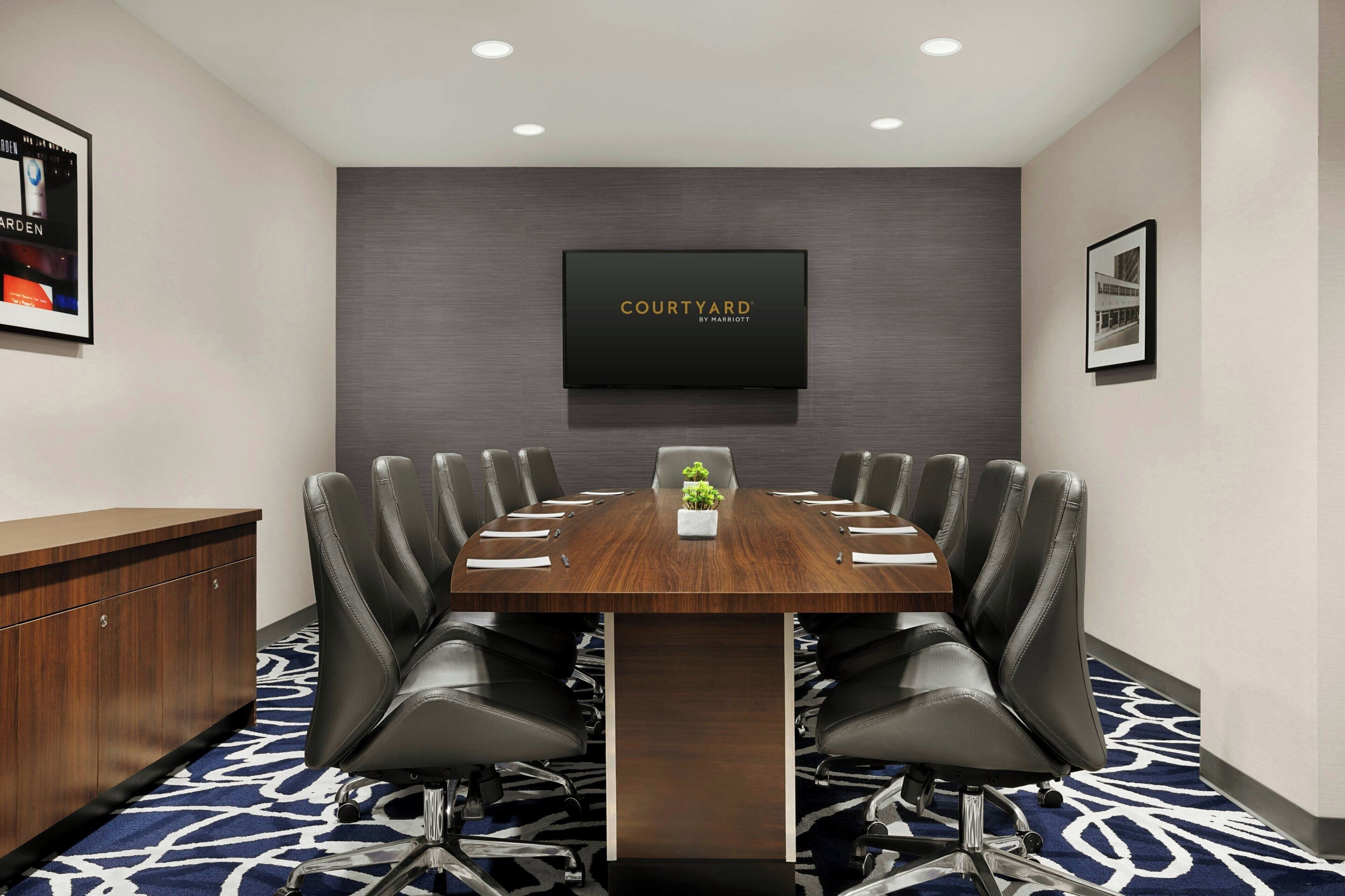 A conference room with a long table, black leather chairs, a small plant, and a 'Courtyard by Marriott' sign on the wall.