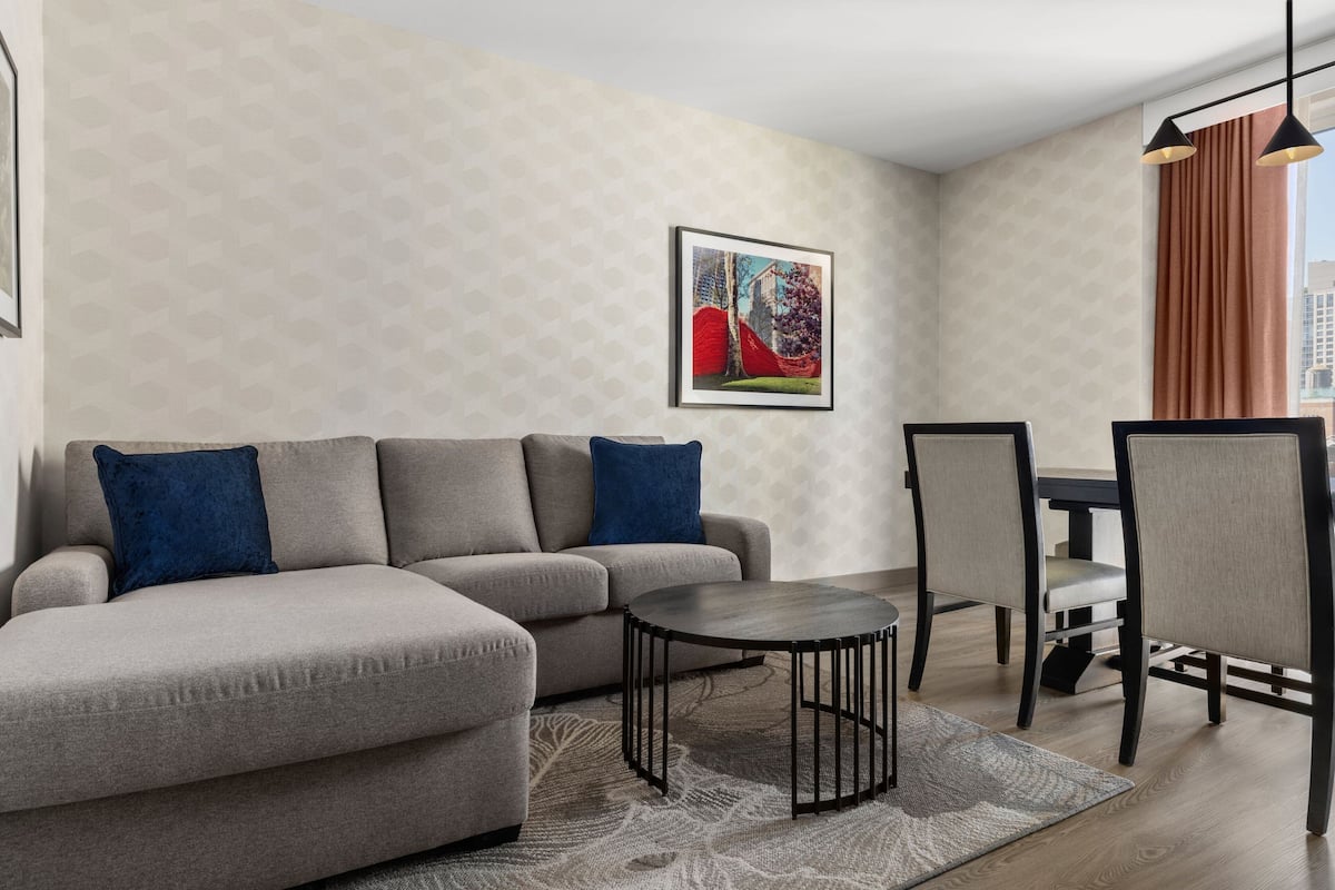 Ein modernes Wohnzimmer mit einem grauen Ecksofa, einem runden Couchtisch und einem Essbereich mit Tisch und Stühlen.