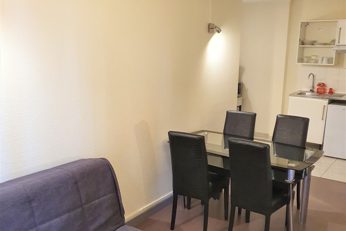 A compact living space with a sofa, a dining table with chairs, and a kitchenette area.