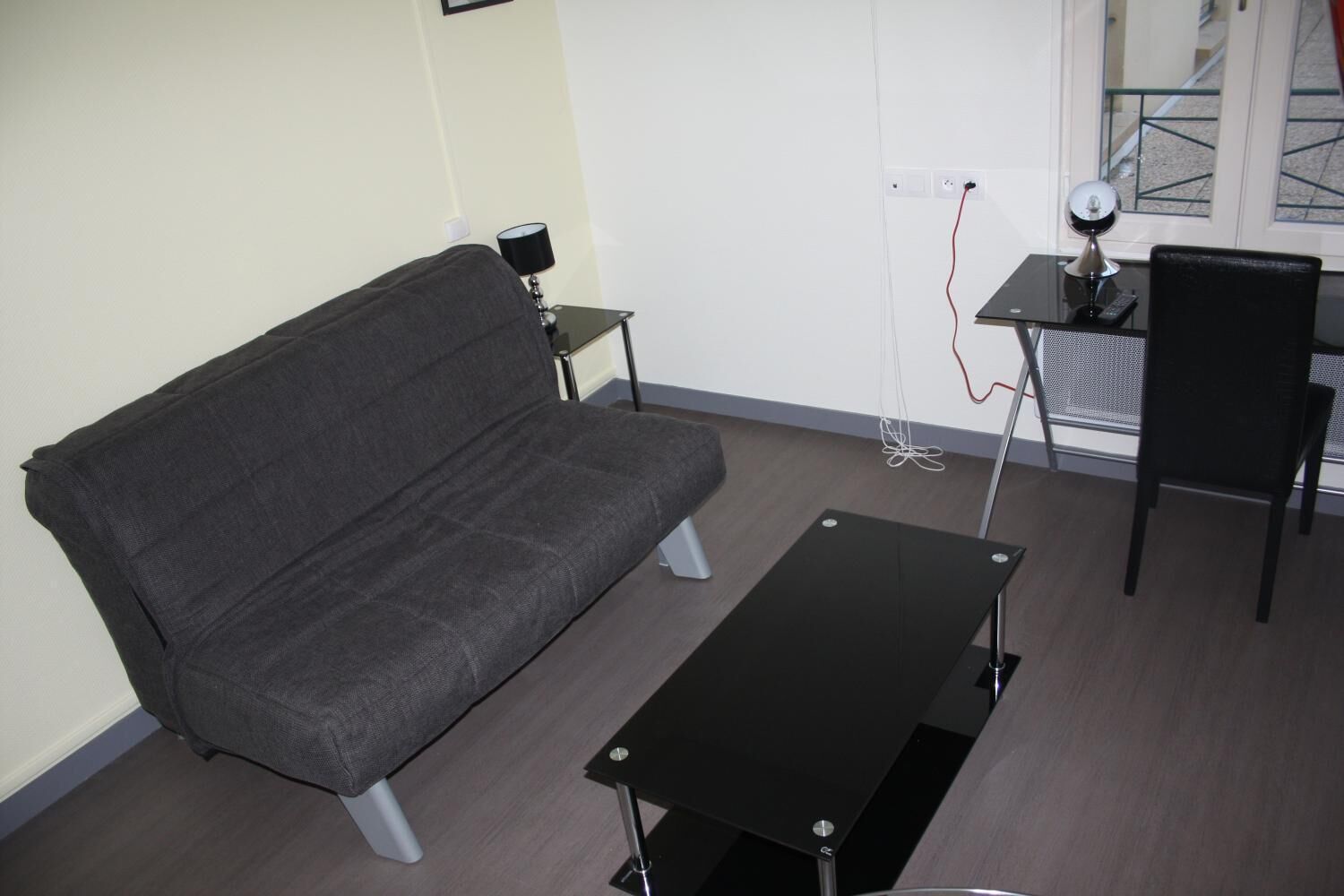 Una sala pequeña con un sofá, una mesita de centro, una mesita con una lámpara y una silla.