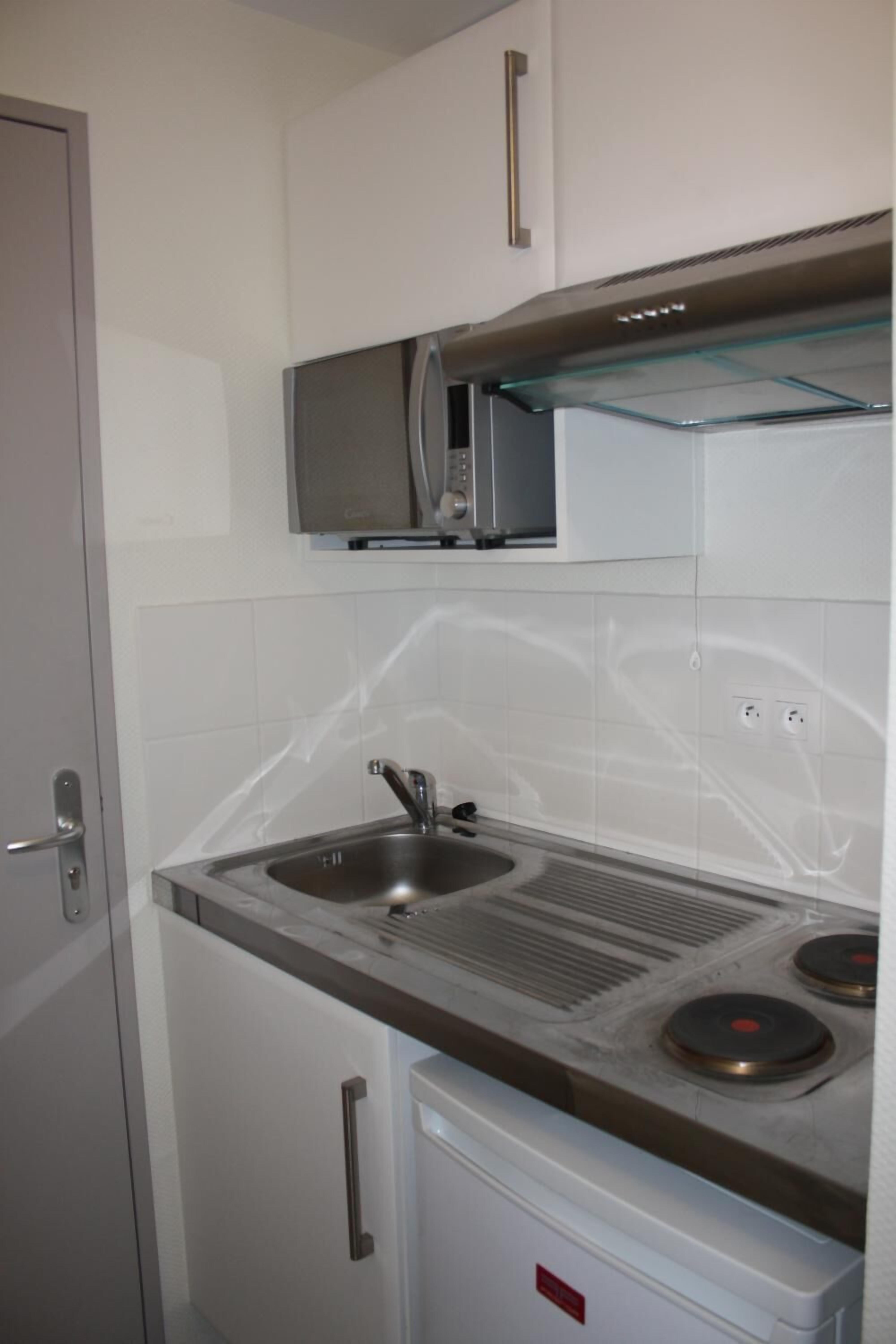 A compact kitchen with a microwave, sink, and a small refrigerator.